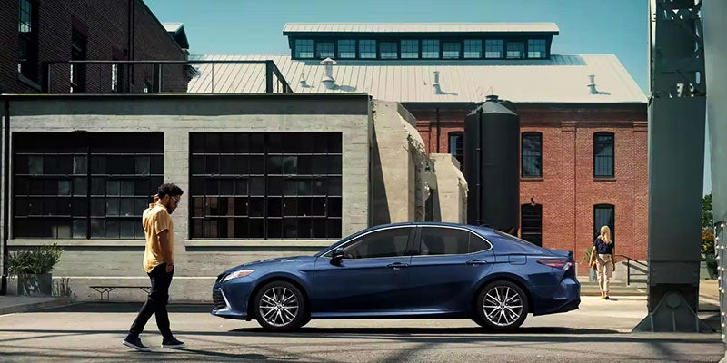 side view of blue Camry parked with a man standing next to it