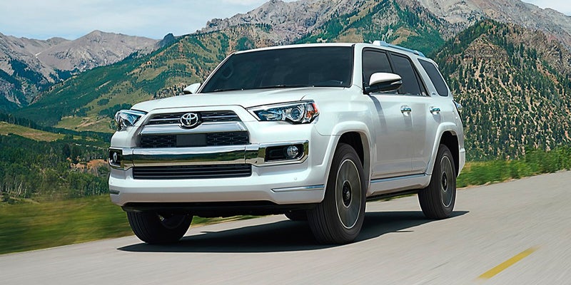 Front right view of a white 2024 Toyota 4Runner drives down a road with mountains in the background