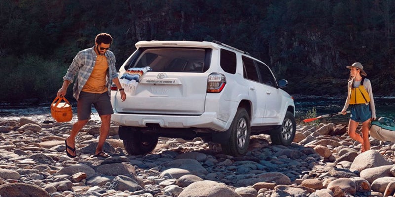 A couple walks away from a white 2024 Toyota 4runner parked on a rocky shoreline