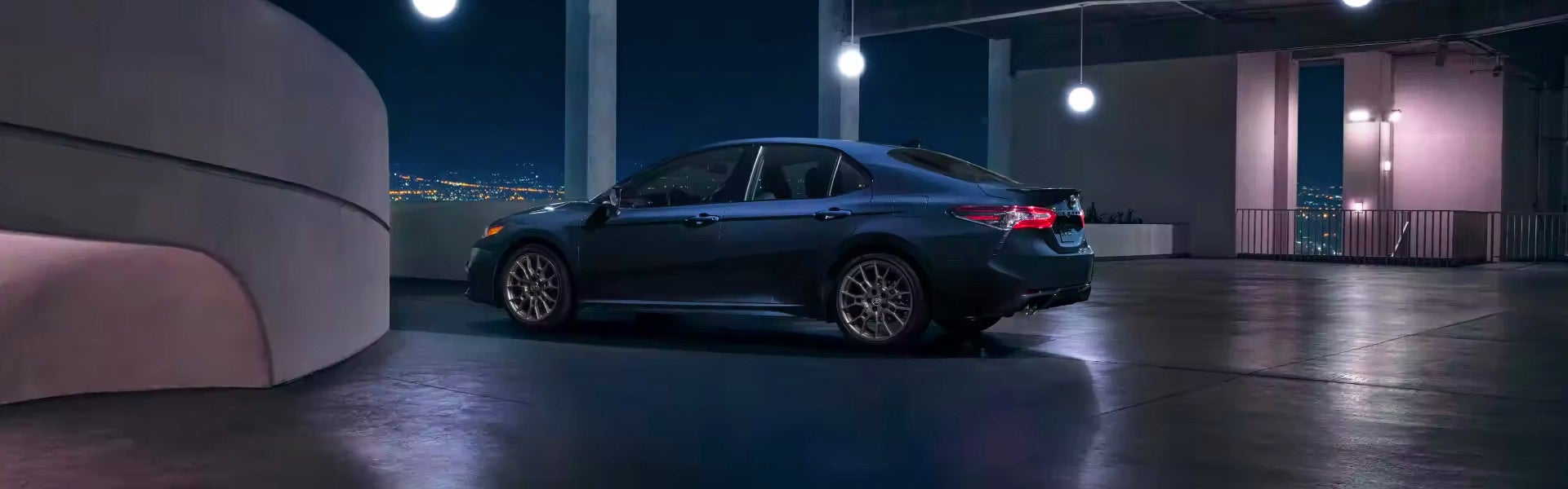 A blue 2024 Toyota Camry Hybrid drives in a parking garage at night.