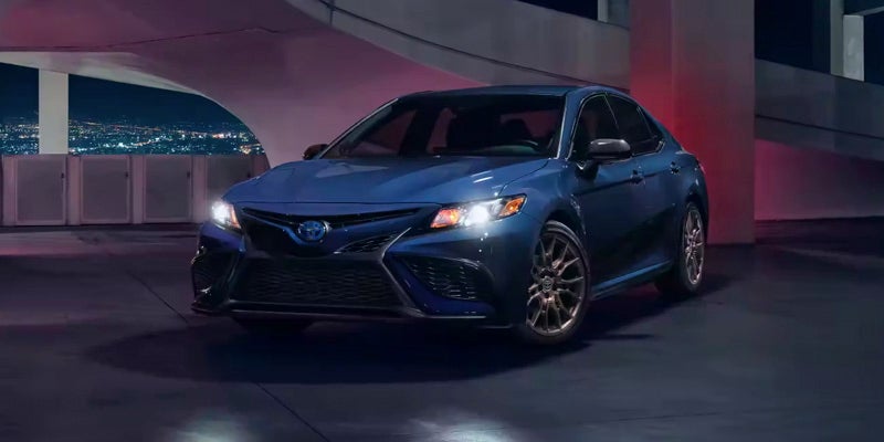 Front right angle view of a navy blue Toyota Camry Hybrid in a parking garage