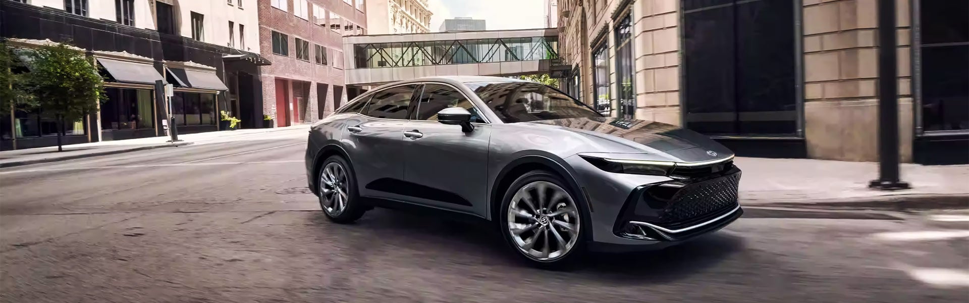 A silver 2024 Toyota Crown drives through a city