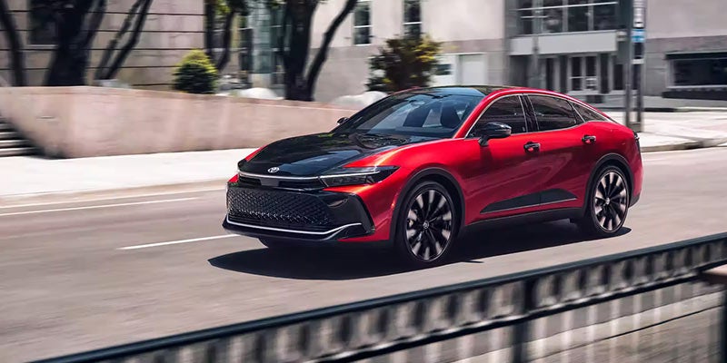Side view of a red 2024 Toyota Crown driving through a city