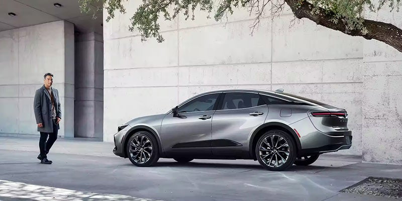 A man walks towards a silver 2024 Toyota Crown parked under a tree