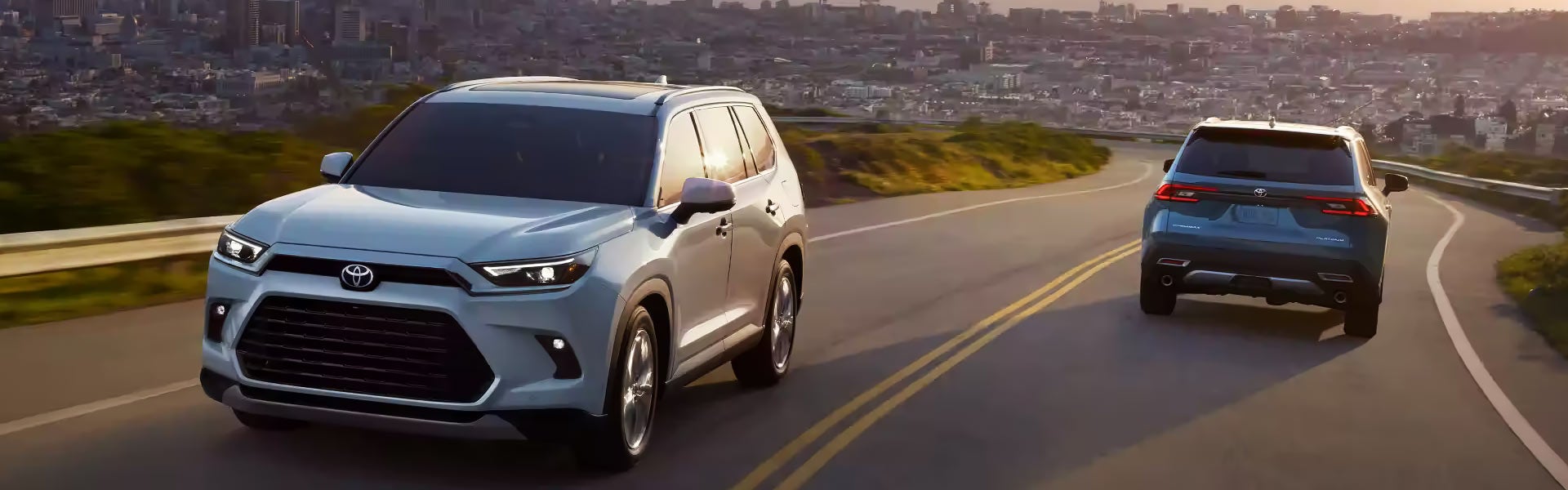 A white 2024 Toyota Grand Highlander drives away from a city