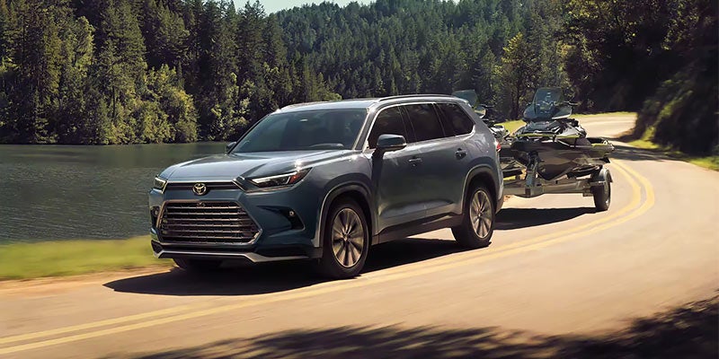 A blue 2024 Toyota Grand Highlander tows a boat