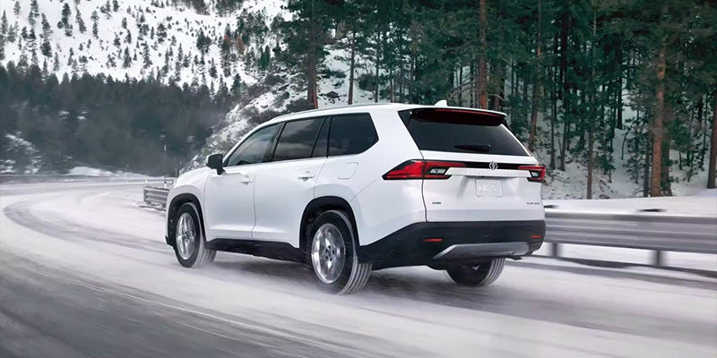 rear view of a white 2024 Toyota Grand Highlander drives down a snowy road