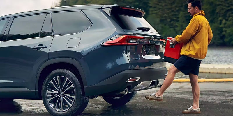 A man opens the trunk of a blue 2024 Toyota Grand Highlander