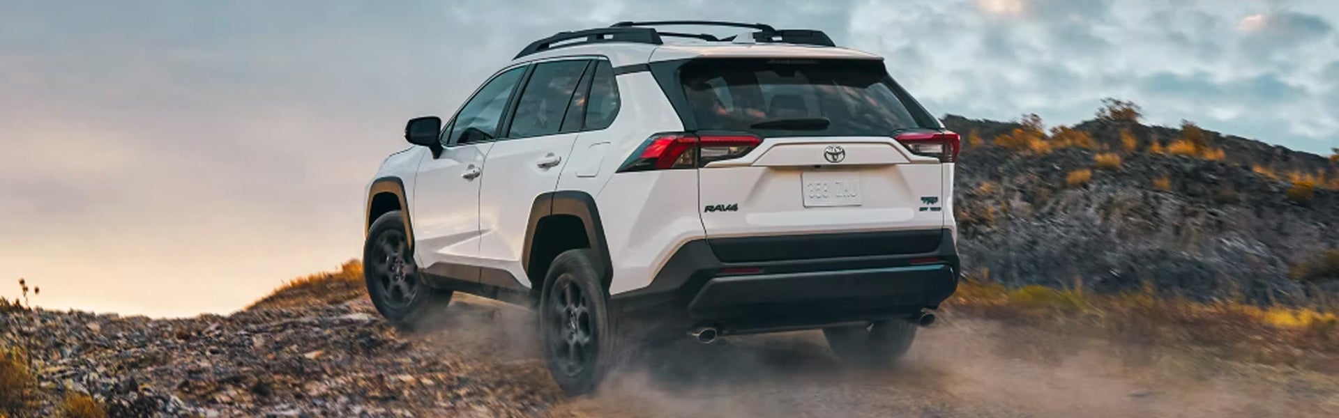 Rearview of a white 2024 Toyota RAV4 driving up a rocky road