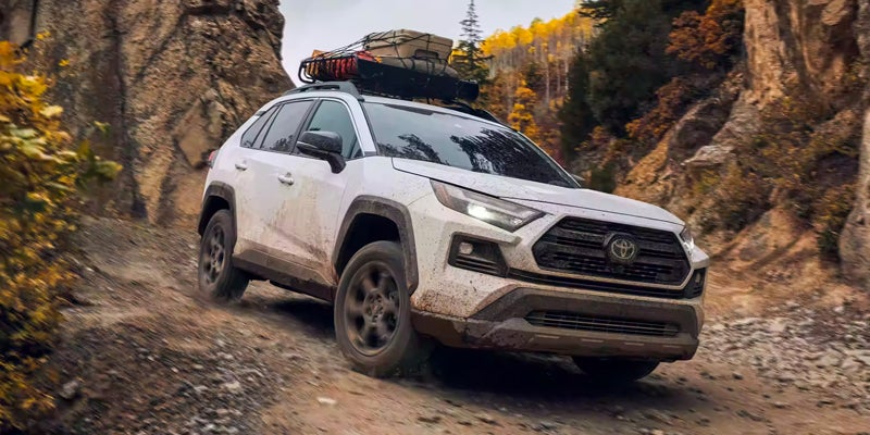 A white 2024 Toyota RAV4 drives down a rocky dirt road