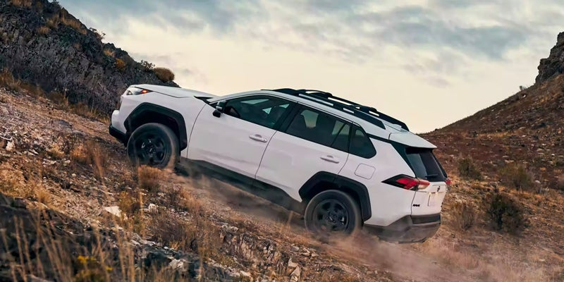 Side view of a white 2024 Toyota RAV4 driving up a dirt road