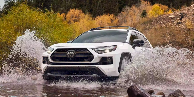 A white 2024 Toyota RAV4 drives through a huge puddle