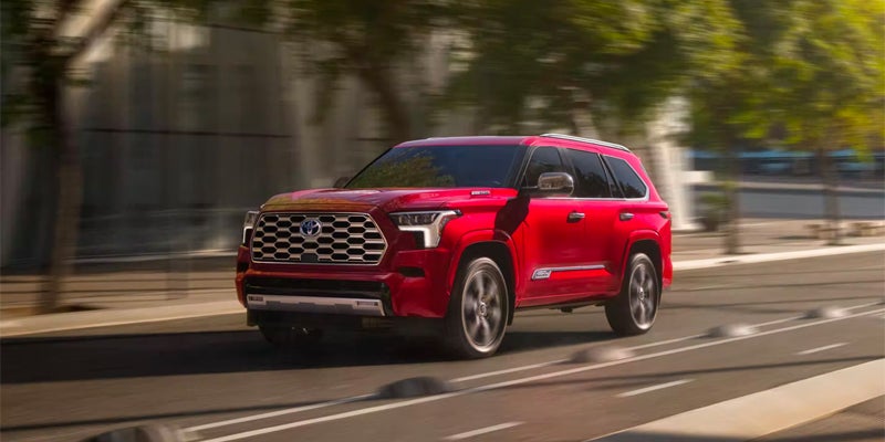 Front right view of a red 2024 Toyota Sequoia driving on a paved road