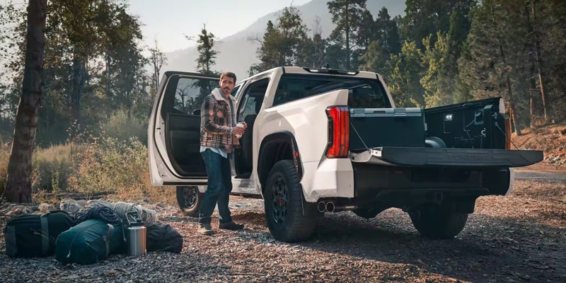 Rear view of a white Toyota Tacoma parked with a man standing next to it and driver side door open
